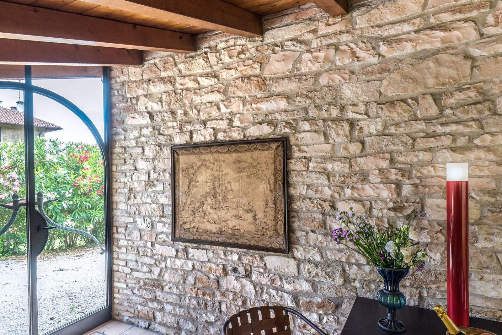 The Loft veranda: a stone wall, a framed tapestry and a glass door onto the garden